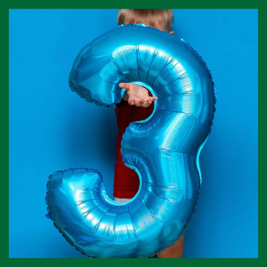 En pojke håller en uppblåst ballong i form av en 3a. Ballongen är blå mot en blå bakgrund. Bilden symboliserar Vetmobilen 3 år.