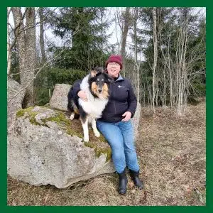 Hunden Zelda och veterinär Agneta sitter på en stor sten. Zelda är en trefärgad collie. 